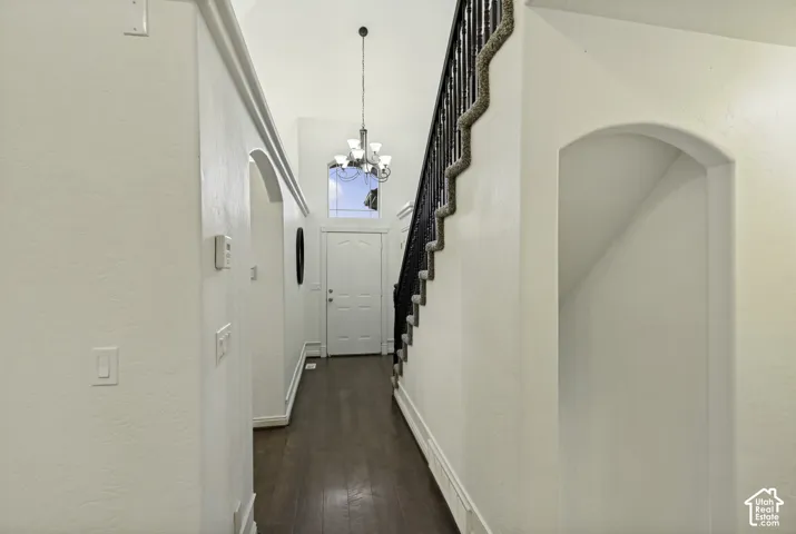 Entryway featuring vaulted ceilings, wood-finish flooring, a tiered chandelier, staircase with a dark-tone banister, and an arched wall cutout