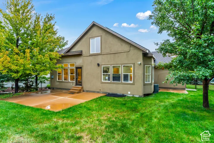 Stucco exterior featuring a concrete patio, gabled roofline, multi-pane windows, and metal perimeter fencing