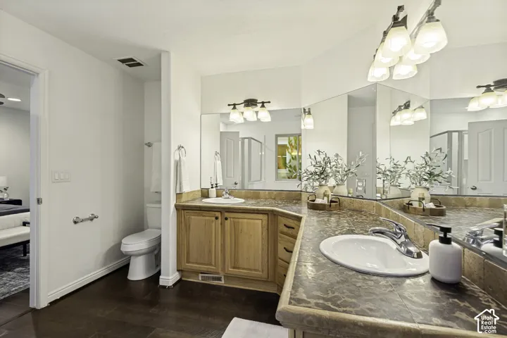 L-shaped vanity with tile countertop, dual recessed oval sinks, natural wood-finish cabinetry, and oversized wall-to-wall mirrors