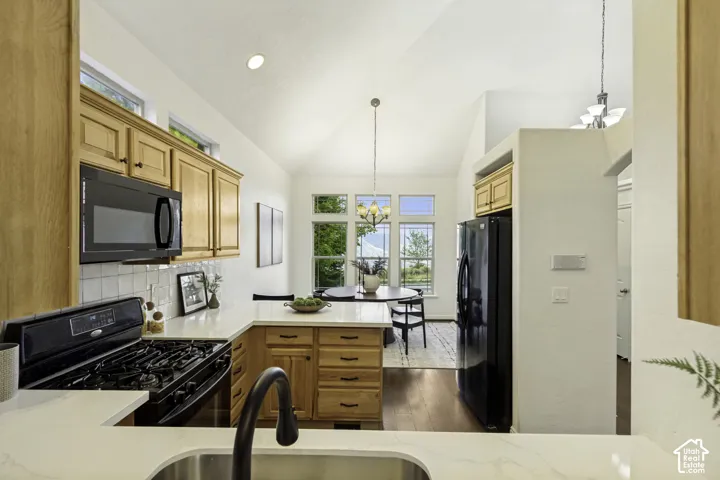 Kitchen featuring vaulted ceilings, light-toned wood cabinetry, stone countertops, and black fixtures