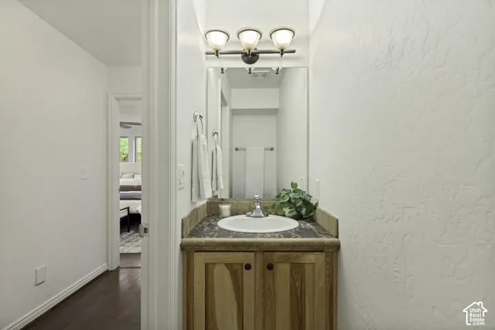 Vanity featuring a natural-finish wood cabinet, stone-finish countertop, integrated round sink, and three-light fixture above a wall-mounted mirror