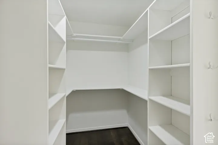 Walk-in closet featuring white built-in shelving, integrated hanging rods, wall-mounted hooks, and wood-finish flooring
