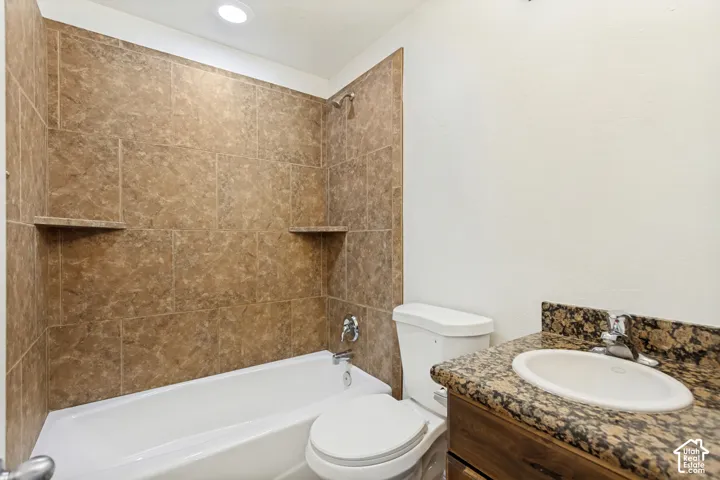 Full-height tiled shower surround with dual built-in corner shelves, integrated bathtub, vanity with stone-finish countertop, and undermount sink
