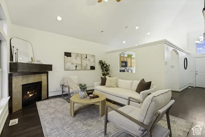 Vaulted ceilings, dark wood-finish flooring, and a fireplace featuring a stone surround and timber mantel