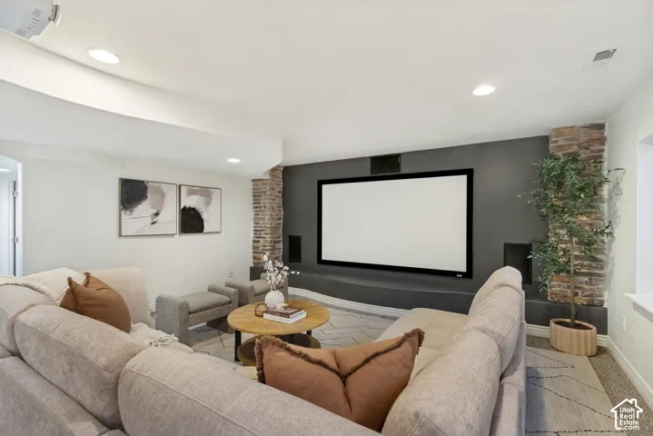 Media room featuring a recessed projection screen, stone-accented columns, a custom built-in low-profile media shelf, integrated wall speakers, and recessed ceiling lighting