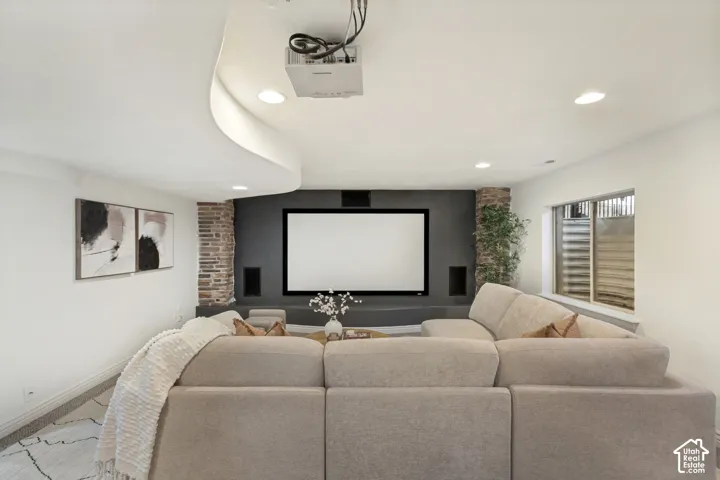 Media room featuring a curved ceiling soffit, recessed lighting, integrated stone column detailing, built-in display shelving, and an installed projection screen