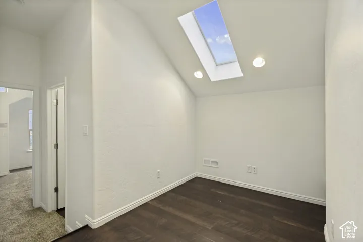 Vaulted ceiling featuring a large rectangular skylight, recessed lighting, and dark wood-finish flooring
