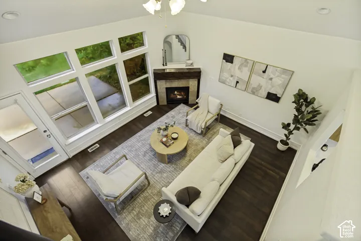 Vaulted ceilings, dark wood-finish flooring, corner fireplace with a stone-tile surround, and expansive multi-pane windows