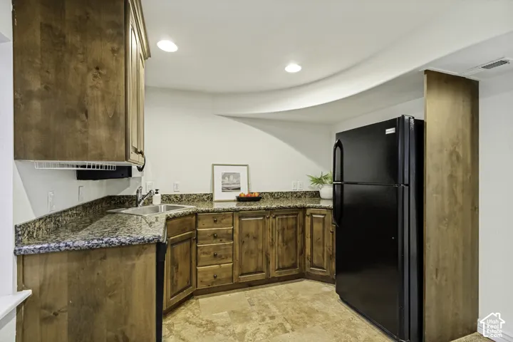 Kitchen featuring stained wood cabinetry, stone-finish countertops, stainless steel sink with a chrome faucet, stone flooring, and a built-in refrigerator enclosure