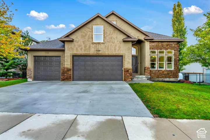 Stucco exterior featuring stacked stone accents, a three-car garage, multi-gabled roofline, and concrete driveway