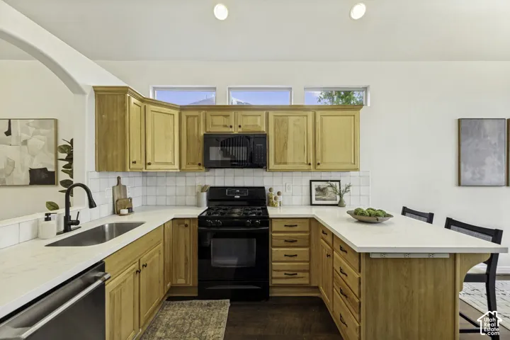 Kitchen featuring wood cabinetry, white countertops, square tile backsplash, black appliances, and triple transom windows