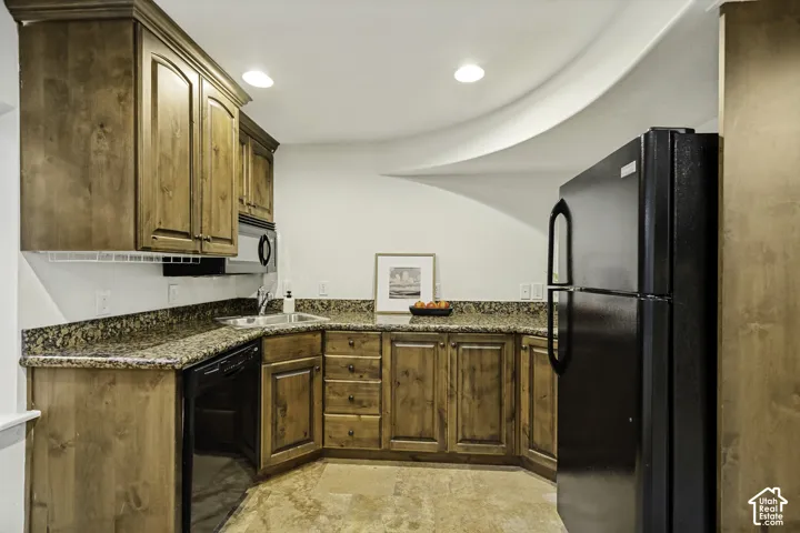 Stained wood cabinetry, stone countertops, recessed lighting, and black appliances