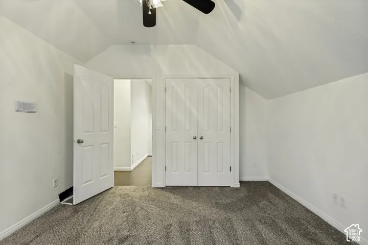 Vaulted ceilings with a neutral color palette, carpeting, built-in double-door closet, and overhead ceiling fan