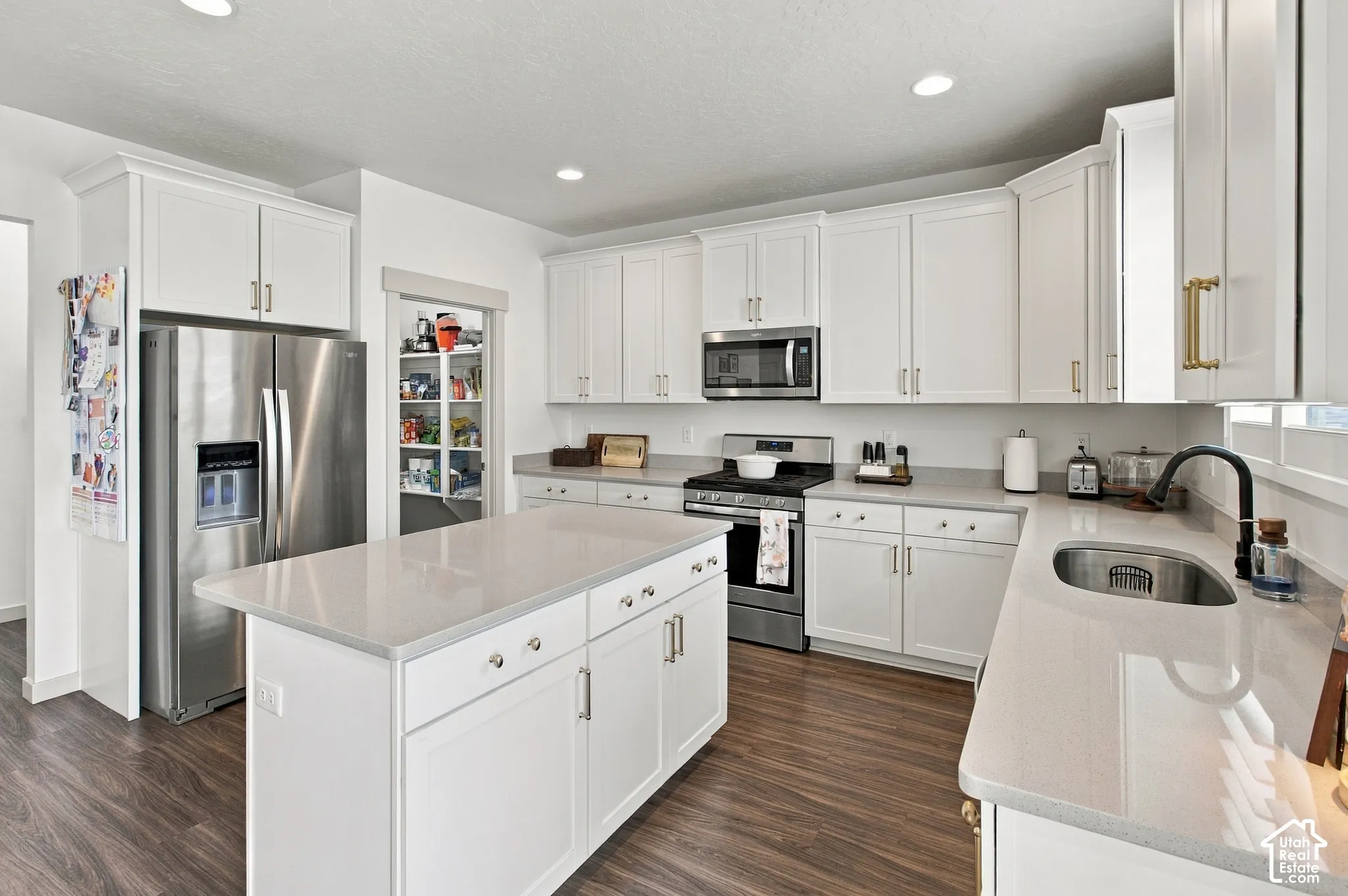 Kitchen featuring white cabinetry, quartz countertops, a center island, stainless steel appliances, and wood-finish flooring