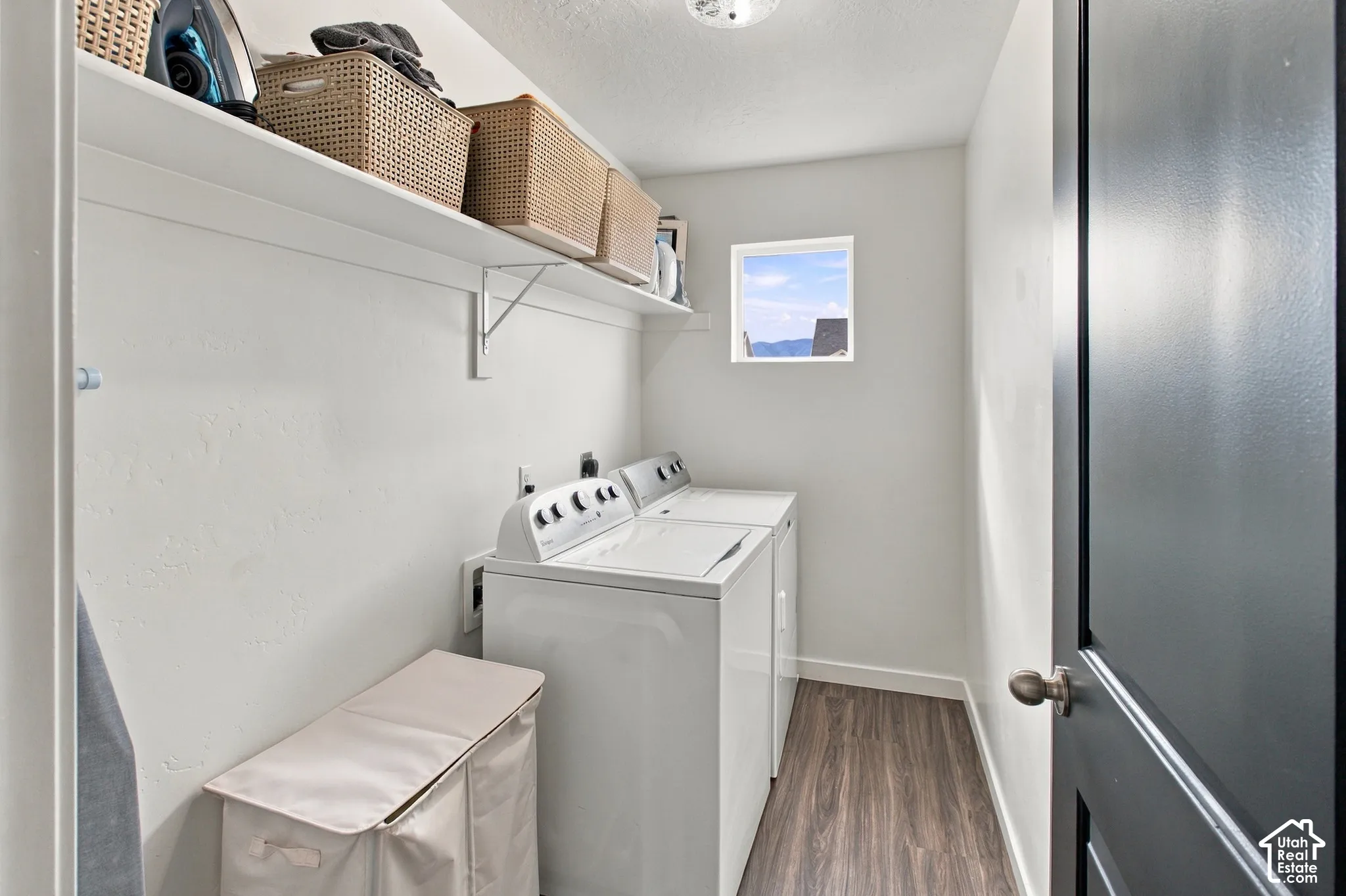 Laundry area featuring wood-finish flooring, white walls, and a high-mounted storage shelf