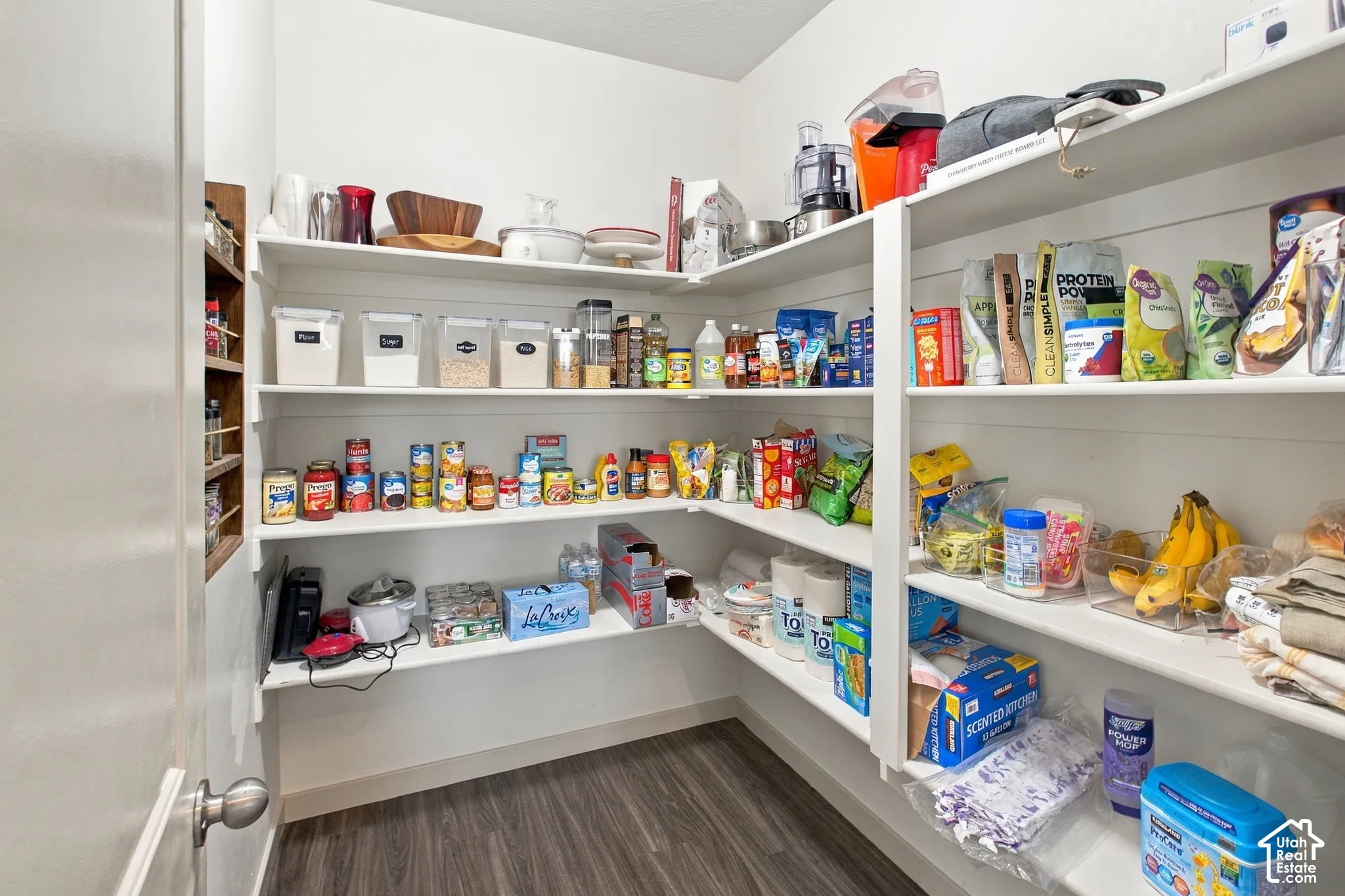 Walk-in pantry featuring white horizontal shiplap wall accents, tiered fixed shelving, and wood-finish flooring