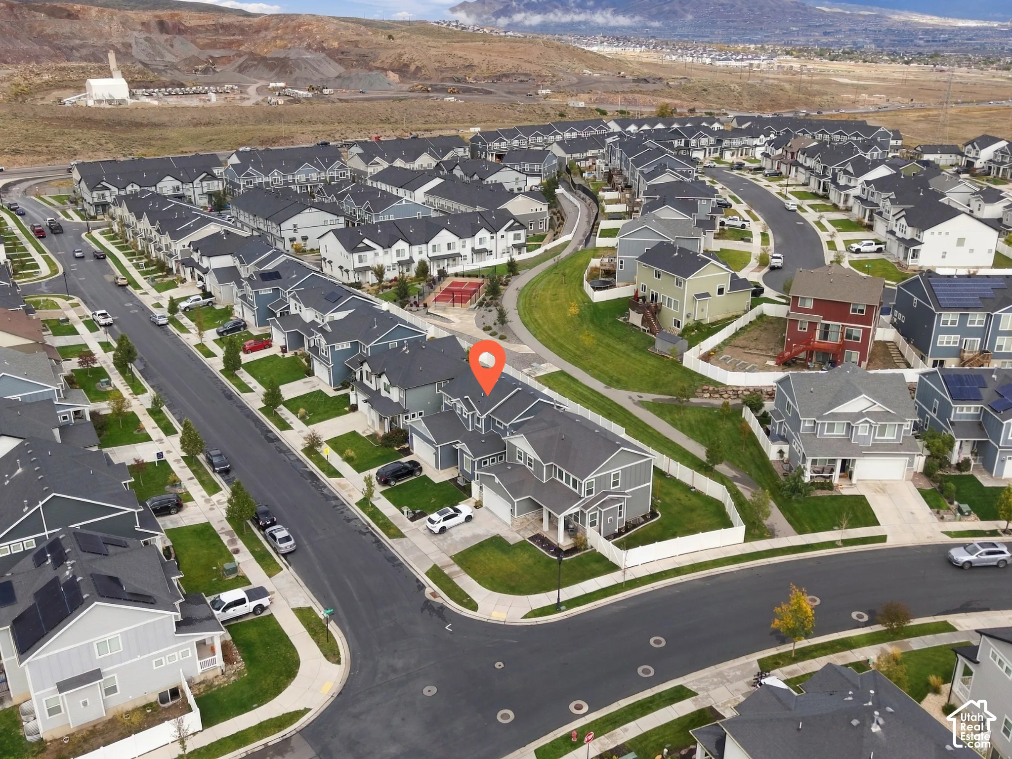 Aerial perspective of a multi-level suburban residence featuring an attached multi-car garage, fenced backyard, asphalt shingle roofing, and paved street access