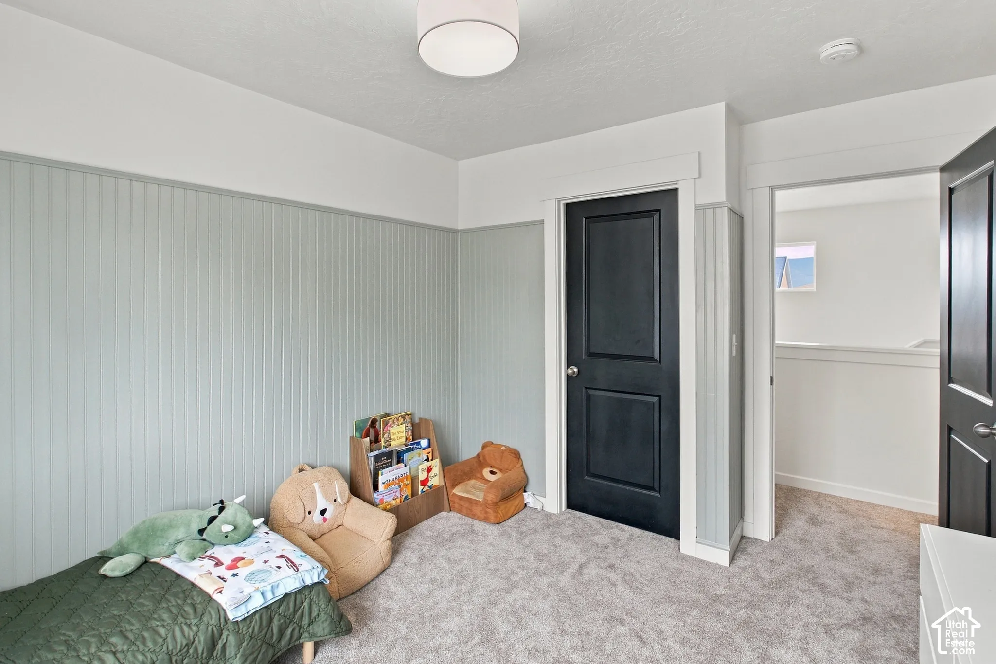 Interior space featuring beadboard wall paneling, neutral carpeting, two black paneled doors, and a flush-mount drum light fixture