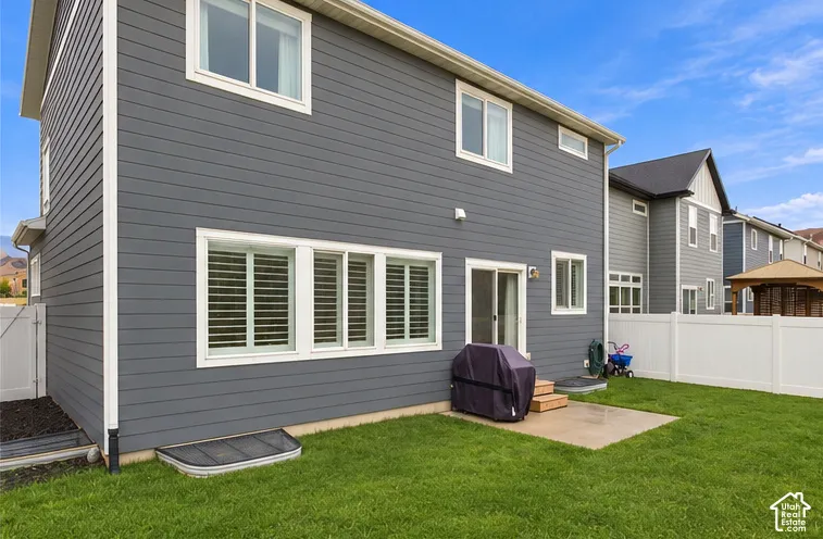 Exterior of the residence featuring dark-toned horizontal siding, a concrete rear patio, multi-pane windows with interior shutters, and a perimeter vinyl privacy fence enclosing a lawn. This image has been digitally altered to remove dust from the rear of