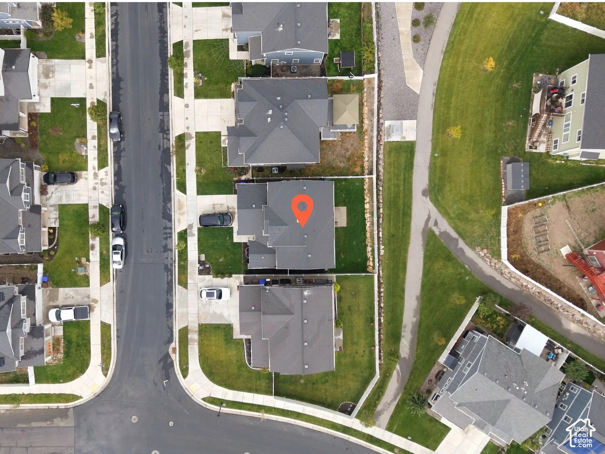 Aerial perspective of a detached residential property featuring a multi-gable roofline, a paved concrete driveway, and a fenced backyard