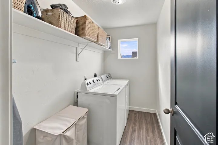 Laundry area featuring wood-finish flooring, white walls, and a high-mounted storage shelf