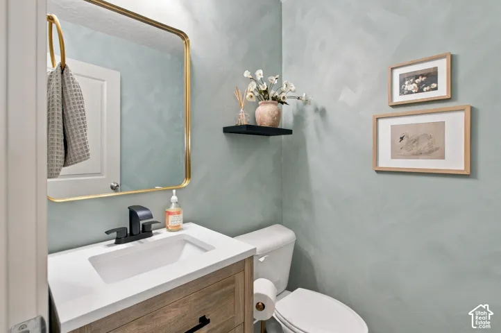 Textured light blue walls, wood-finish vanity with a white countertop, rectangular undermount sink, matte black faucet, and brass-framed mirror
