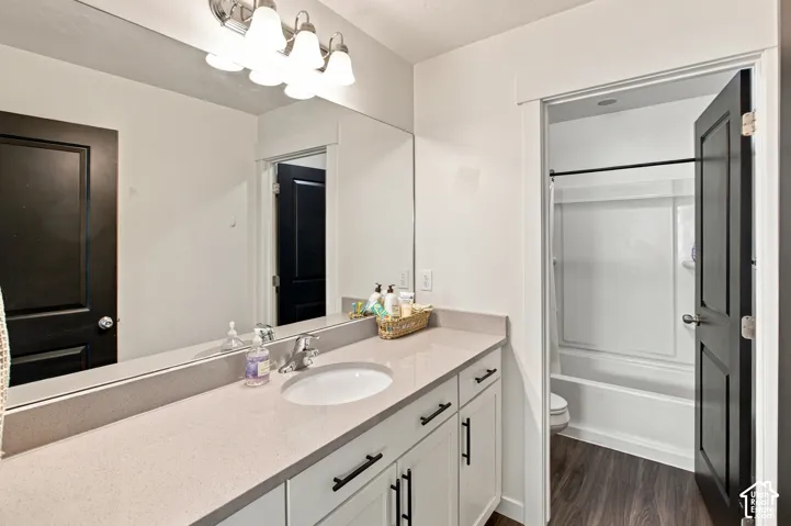 Bathroom featuring a solid-surface countertop, white cabinetry with matte black hardware, a full-width vanity mirror, polished chrome faucet, and wood-finish flooring