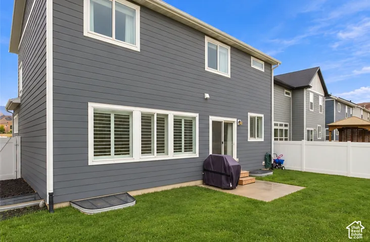 Exterior of the residence featuring dark-toned horizontal siding, a concrete rear patio, multi-pane windows with interior shutters, and a perimeter vinyl privacy fence enclosing a lawn. This image has been digitally altered to remove dust from the rear of