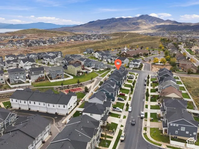 Aerial perspective of a multi-unit residential property featuring dark-toned roofing, concrete driveway surfaces, and a backdrop of mountain scenery