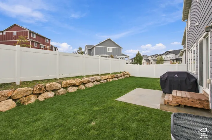 Backyard featuring a white vinyl privacy fence, natural stone retaining wall, concrete patio, and lawn area