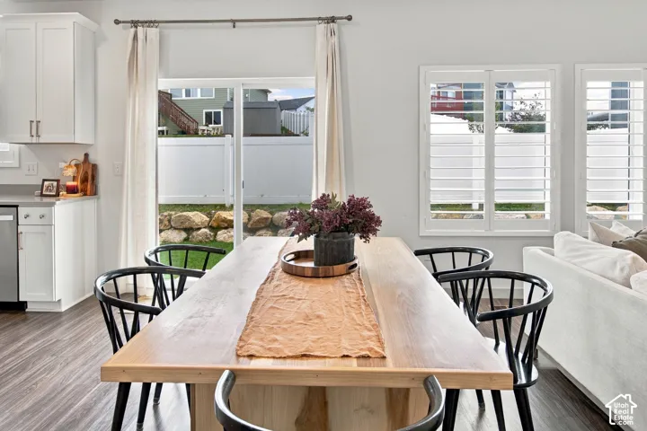 Dining area featuring wood-finish flooring, white shaker-style cabinetry, plantation shutters, and sliding glass door access to the rear yard