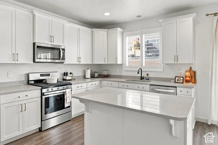 Kitchen featuring white shaker-style cabinetry, quartz countertops, stainless steel appliances, a central island, and wood-finish flooring