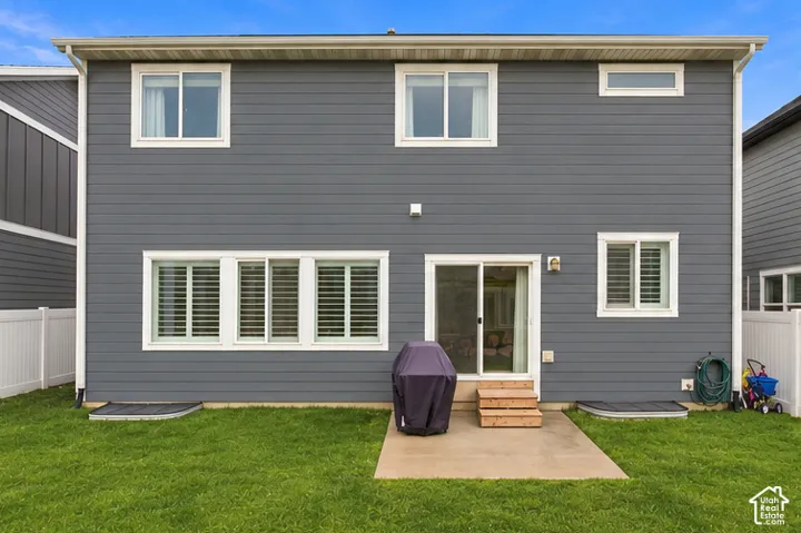 Two-story residential exterior featuring dark horizontal siding, sliding glass door, concrete patio, multi-pane windows, and white vinyl privacy fencing. This image has been digitally altered to remove dust from the rear of the house. Real-time conditions