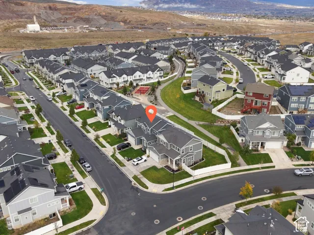 Aerial perspective of a multi-level suburban residence featuring an attached multi-car garage, fenced backyard, asphalt shingle roofing, and paved street access