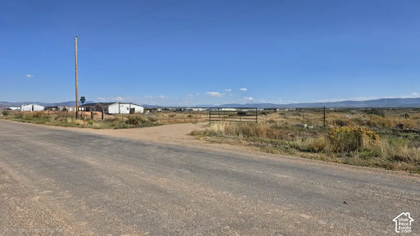 Expansive land parcel featuring a gravel road frontage, metal pipe fencing, and mountain horizon backdrops