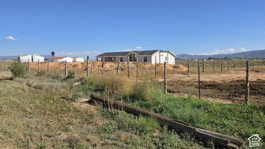 Single-level residence with a gabled roofline and an expansive lot featuring mountain range scenery and perimeter wire fencing
