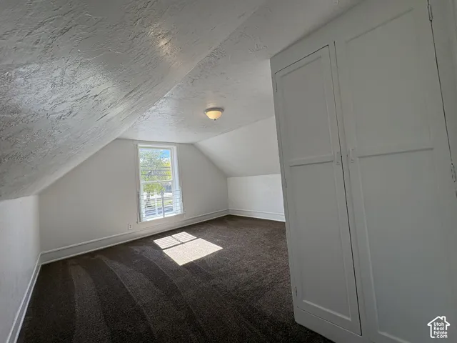 Finished attic space featuring vaulted ceilings, built-in cabinetry, carpeting, and a single window