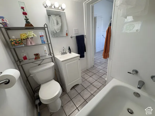 Bathroom featuring tile flooring, a white vanity cabinet with an integrated sink, a multi-bulb vanity light fixture, and a built-in bathtub with wall-mounted plumbing hardware
