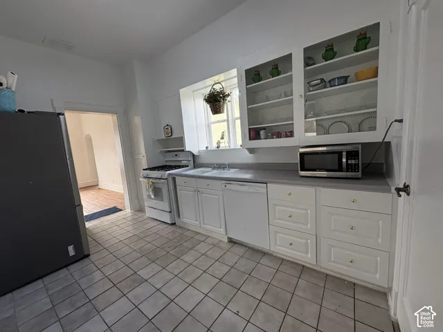 Kitchen featuring white cabinetry, integrated glass-front display shelving, tile flooring, and solid surface countertops