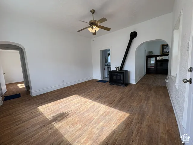 Living space featuring wood-finish flooring, a freestanding black stove, arched thresholds, and a ceiling fan with integrated lighting