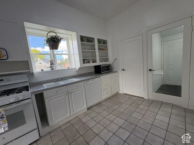 Kitchen featuring white cabinetry, integrated glass-front display shelving, solid-surface countertops, tile flooring, and a glass-panel door