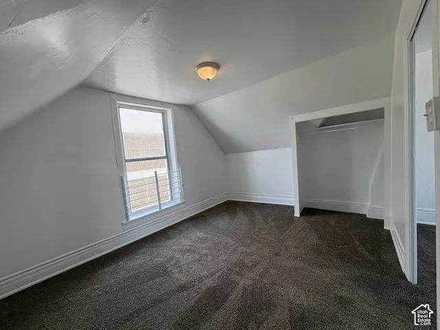 Sloped ceiling architecture featuring neutral-toned carpeting, a built-in recessed closet, and a single-hung window with a security bar