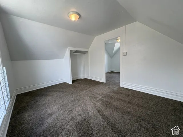 Vaulted ceiling room featuring neutral carpeting, a built-in recessed storage alcove, and a flush-mount ceiling light fixture