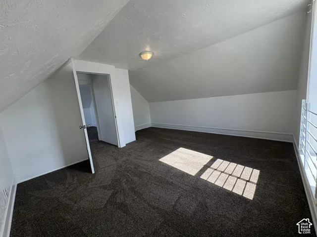 Interior room featuring vaulted ceilings, textured wall surfaces, neutral carpeting, and a flush-mount ceiling fixture