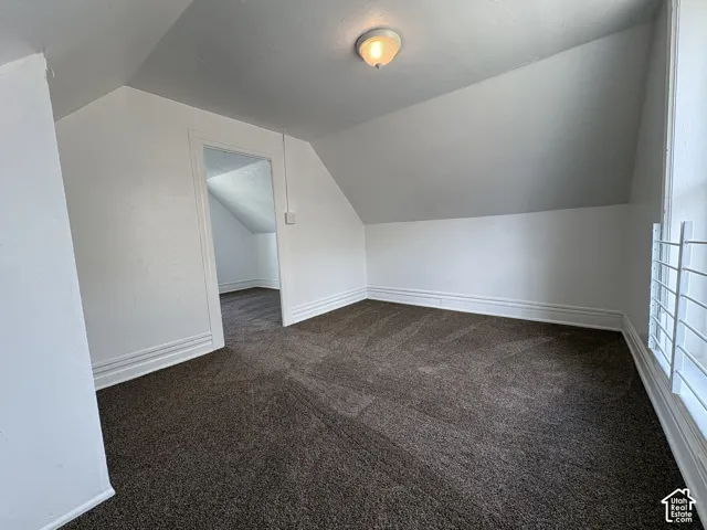 Room with angled ceiling, carpeted flooring, neutral wall paint, and ceiling-mounted light fixture