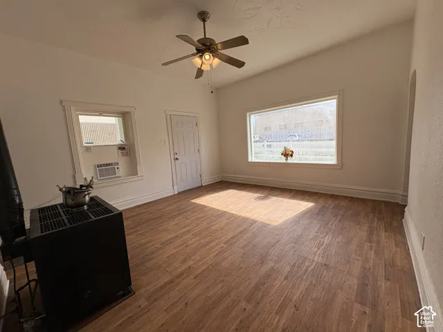 Interior space featuring wood-finish flooring, a large picture window, a ceiling fan with integrated lighting, and a solid-fuel stove