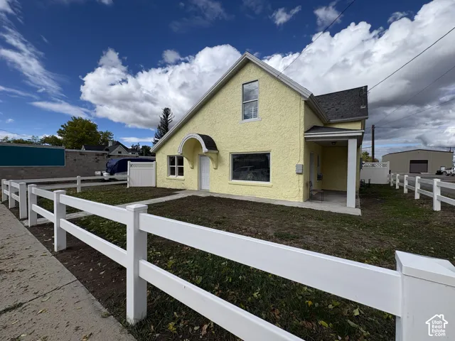 Textured stucco exterior featuring a gabled roofline, decorative arched entry canopy, covered porch with square columns, and white vinyl perimeter fencing