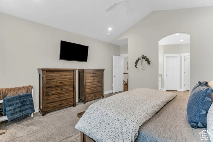 Vaulted ceiling featuring a central paddle fan, neutral wall paint, and an arched doorway with paneled interior doors