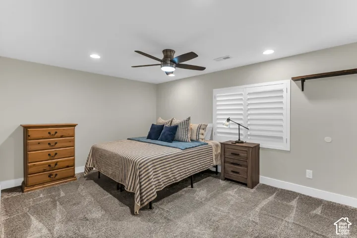 Neutral-toned interior featuring recessed lighting, a modern ceiling fan, wall-mounted white plantation shutters, and a fixed wooden wall shelf