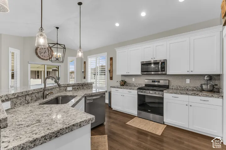 Kitchen featuring white cabinetry, stone-surface countertops, stainless steel appliances, wood-finish flooring, and pendant lighting